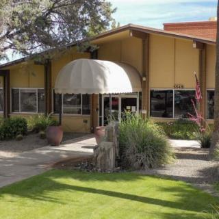A building entrance with a canopy, surrounded by greenery and trees.