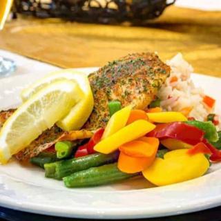 A plate featuring grilled fish served with a colorful mix of vegetables and garnished with lemon slices.