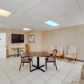 A spacious and well-lit waiting room featuring a table, chairs, and a television.