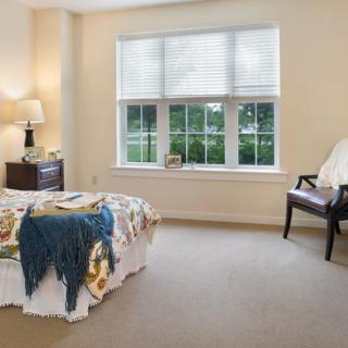 A cozy bedroom with a large window, bed, chair, and bedside lamp.