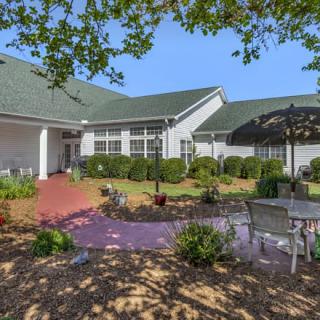 A sunny patio area outside a building, featuring outdoor seating and lush landscaping.
