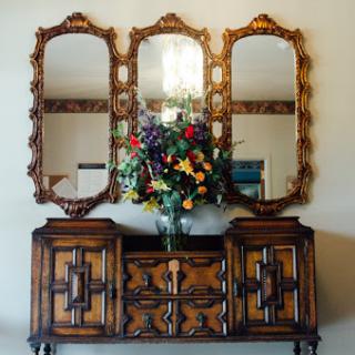 A beautifully crafted wooden cabinet with a decorative floral arrangement, complemented by an elegant triple mirror.