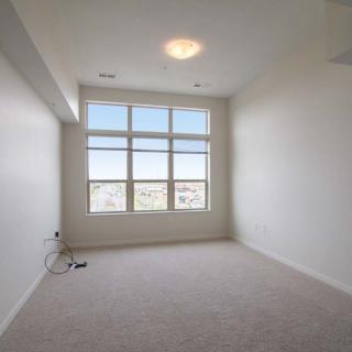 A minimalist empty room with a large window and carpeted floor.