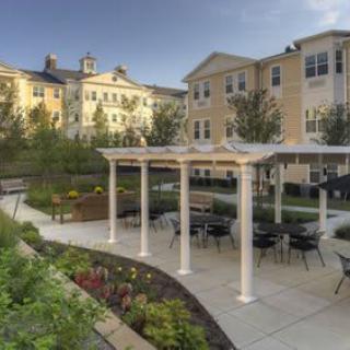 A beautifully landscaped outdoor seating area with a pergola in front of an apartment building.