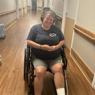 A person sitting in a wheelchair wearing headphones and smiling in a hallway.