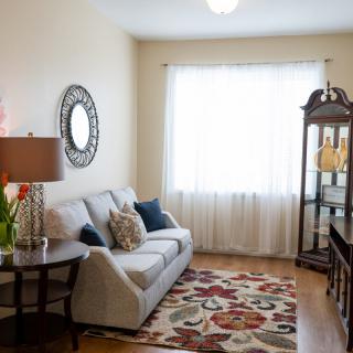 A cozy and decorated living room featuring a sofa, colorful rug, and a sunlit window.