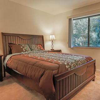 A cozy bedroom with a wooden bed, bedside lamp, and a window with natural light.