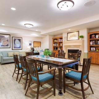 A modern dining area with a large table surrounded by chairs, featuring bookshelves and a fireplace.