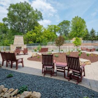 A serene outdoor space featuring a patio with wooden chairs, surrounded by lush greenery and a fireplace.