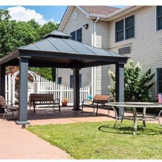 A cozy outdoor patio area with a gazebo, benches, and a table set in the garden beside a house.