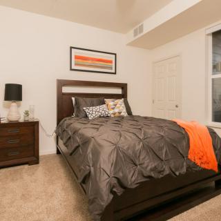 A modern bedroom with a neatly made bed, featuring dark furniture and colorful accents.