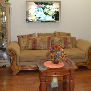 A cozy living room with a sofa, coffee table with a flower arrangement, and a TV mounted on the wall.
