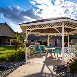 A sunny day in a residential garden featuring a white gazebo with patio furniture.