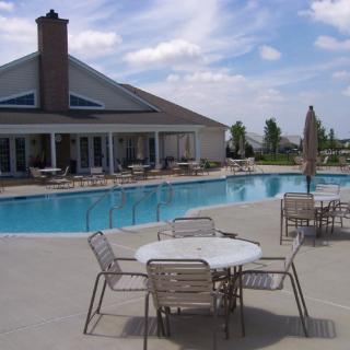 A view of a residential swimming pool with patio furniture and a clubhouse on a sunny day.