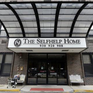 Entrance of The Selfhelp Home with a glass canopy and seating area.