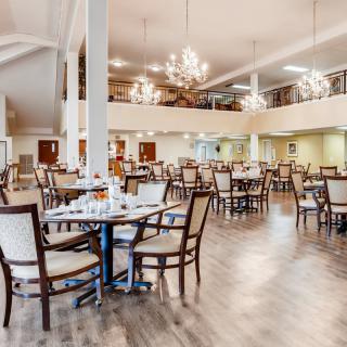 A spacious dining area with neatly arranged tables and chairs, illuminated by elegant chandeliers.