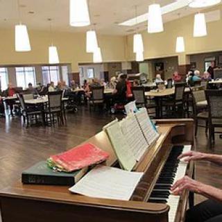 A pianist plays in a dining hall with people seated at tables.