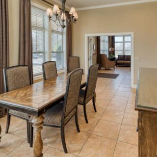 A dining room with a wooden table and chairs, featuring large windows and a chandelier.