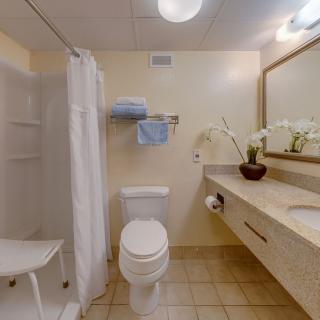 A clean and well-organized bathroom featuring a shower, toilet, sink, and mirror, with towels neatly arranged on a rack.