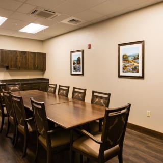 A well-lit conference room with a large wooden table and chairs, adorned with framed artwork on the walls.