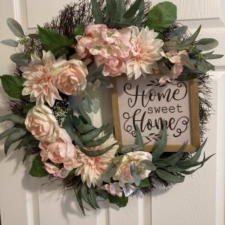 A decorative wreath with pink flowers and greenery surrounding a 'Home Sweet Home' sign.