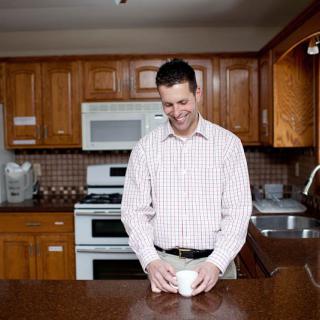 A man smiling while holding a cup in a kitchen.