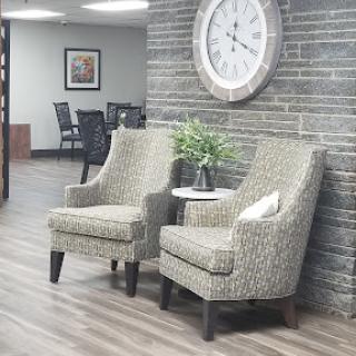 A cozy waiting area featuring two patterned chairs, a small table with a decorative plant, and a large wall clock.