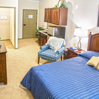 A cozy bedroom featuring a striped blue bedspread, wooden furniture, and a patterned armchair.