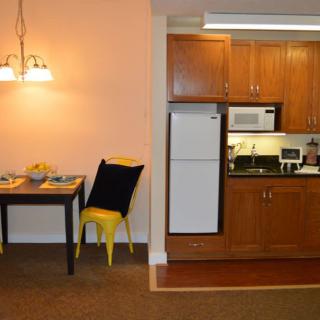 A cozy kitchen and dining area featuring wooden cabinets, a refrigerator, microwave, and a dining table with bright yellow chairs.