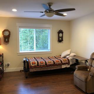 A cozy bedroom with a single bed, recliner, wall clocks, and a ceiling fan.