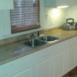 A kitchen with a double sink, countertop, and cabinets beneath a window with blinds.