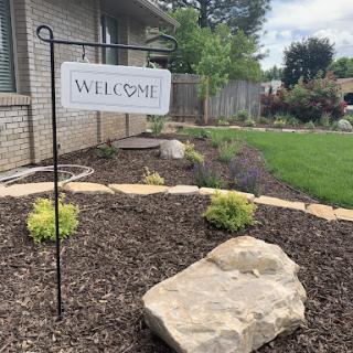 A welcoming sign in a beautifully landscaped garden area.
