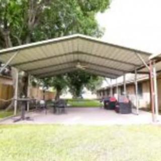 A spacious outdoor patio area with a metal canopy, furnished with tables and chairs, surrounded by greenery.