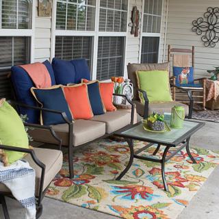 A cozy outdoor patio with colorful pillows, a patterned rug, and various furniture pieces.