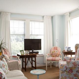 A cozy living room with floral furniture and large windows allowing natural light.