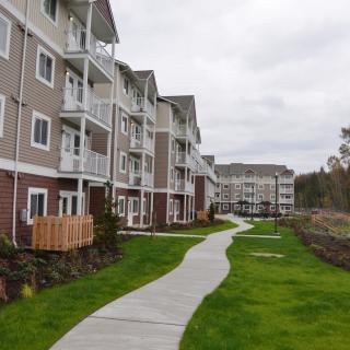A row of modern apartment buildings with a winding sidewalk bordered by green grass.