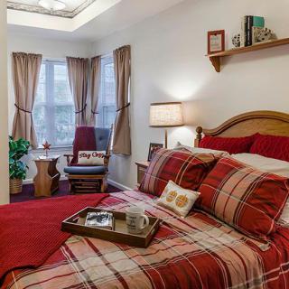 A cozy bedroom with red plaid bedding, a window with curtains, and a chair in the corner.