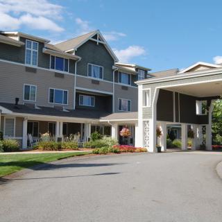 An exterior view of a multi-story residential building with a covered entrance and landscaped surroundings.