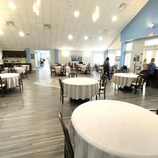 A spacious restaurant interior with round tables and ample natural lighting.