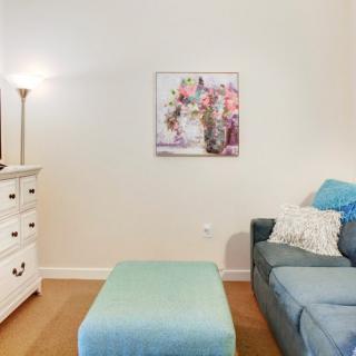 A cozy living room corner with a sofa, ottoman, dresser, and wall art.