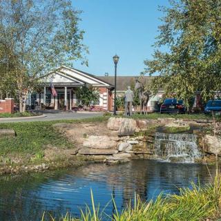 A picturesque view of a small waterfall cascading into a serene pond near a building surrounded by trees.