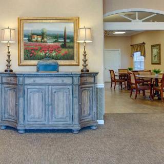 A well-decorated lobby area featuring a wooden cabinet with lamps, a landscape painting, and a dining area in the background.