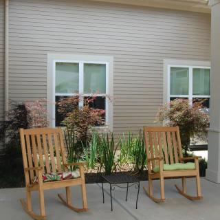 A cozy patio setup with wooden rocking chairs and plants against a building exterior.