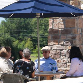 A group of people sitting under an umbrella on a patio, engaged in conversation.
