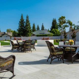 A spacious outdoor patio with wicker furniture, surrounded by a garden and trees on a sunny day.