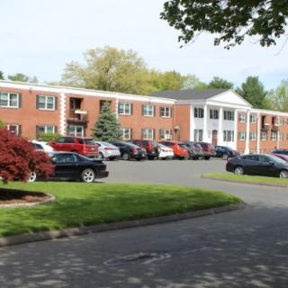 A suburban apartment building with a parking lot and surrounding trees.