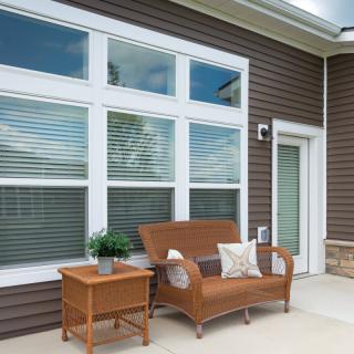 A cozy patio area with a wicker bench and side table in front of large windows.