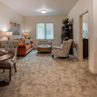 A cozy living room featuring a sofa and armchairs, with a dining table in the foreground and decorative elements throughout.