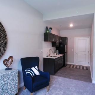 A cozy and modern apartment living area with a kitchenette, featuring minimalist decor and comfortable seating.