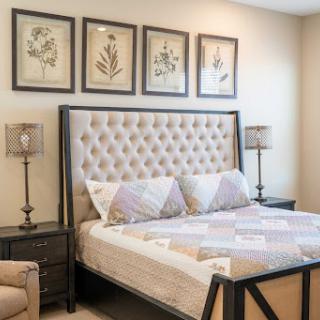 A cozy and modern bedroom featuring a tufted bed, elegant lamps, and framed botanical art.